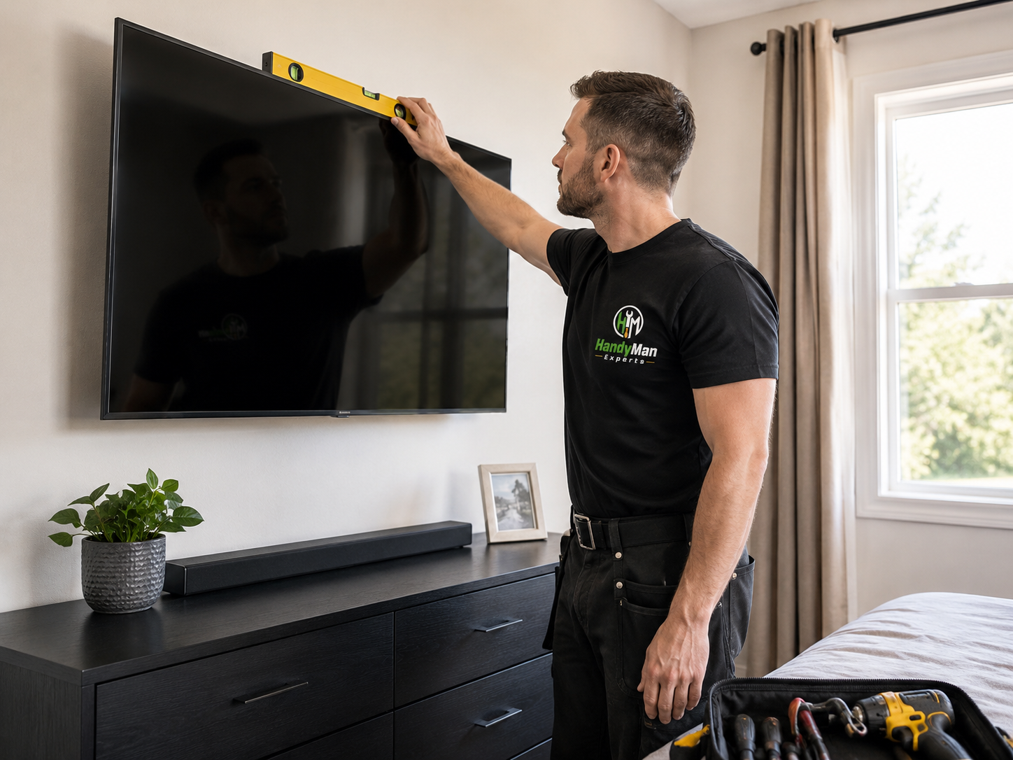 Handyman Experts technician leveling a wall-mounted TV in a bedroom